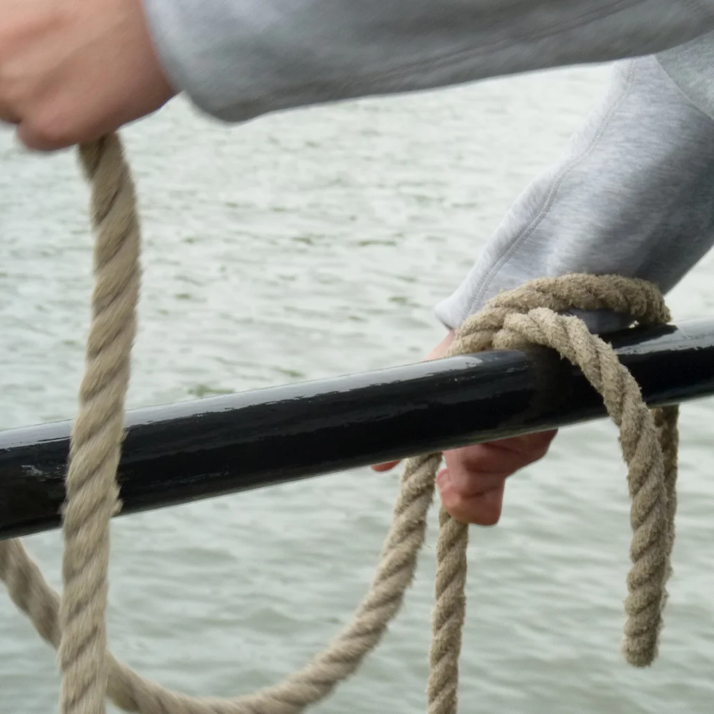 Hände, die ein dickes Tau um ein Geländer am Wasser wickeln