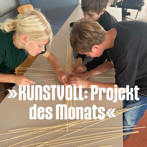 Drei Kinder beugen sich über einen Tisch und bauen gemeinsam ein filigranes Gerüst aus langen Holzstäben.